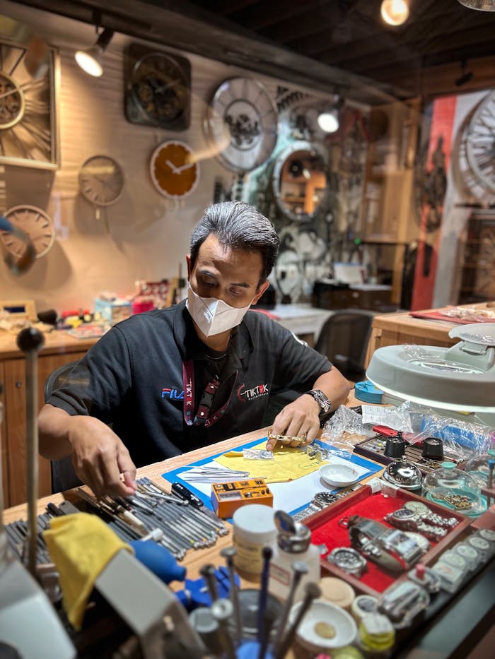 Watchmaker in an Indonesian studio working meticulously on watches, surrounded by tools.